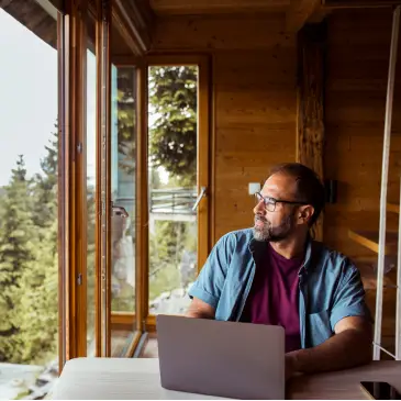 Remote worker sitting at desk with laptop in a remote wooded area.